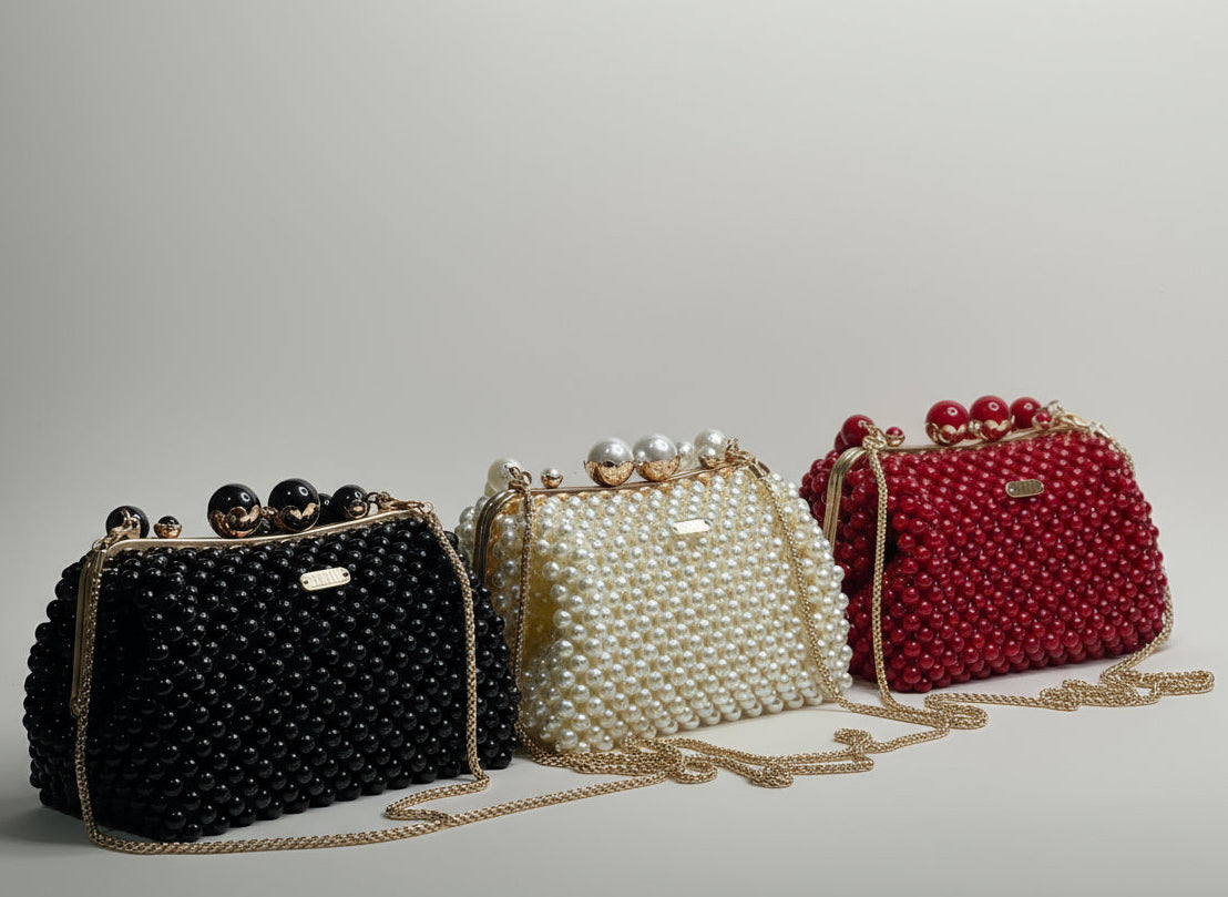 Three handbags with black, pearl, and red bead embellishments on a white surface with a plant in the background.